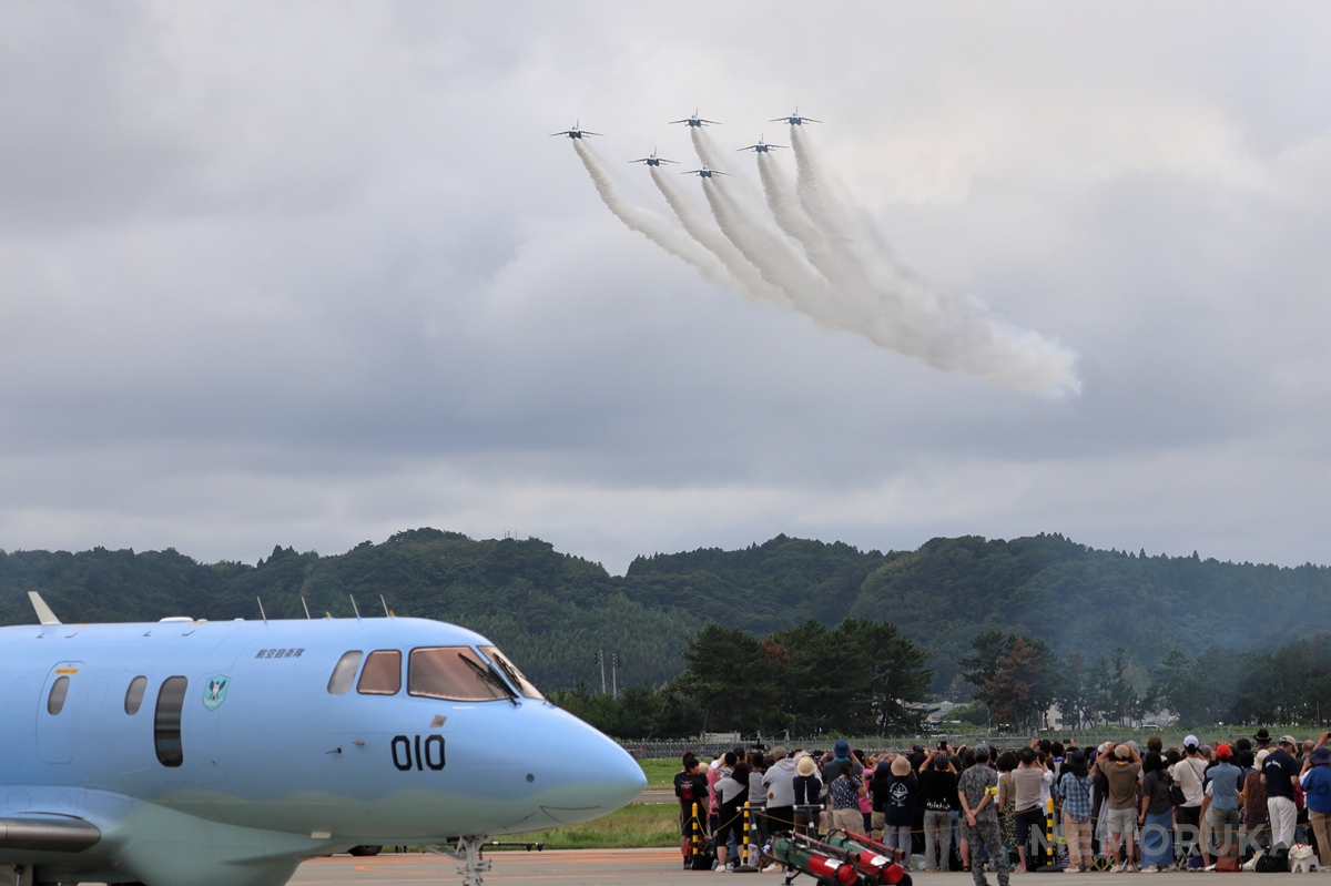 上空を飛行するブルーインパルスと、夢中で空を見上げる観客